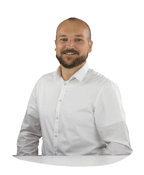 Michael Binder stands behind a table in a white shirt and looks into the camera with a smile.